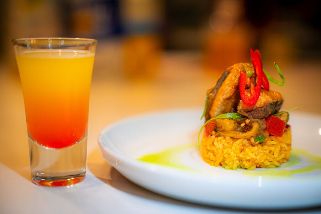 A vibrant showcase of Filipino flavors: Bangus ala Pobre served with fragrant garlic rice and tangy eggplant salad, beautifully complemented by a refreshing Calamansi Sunset Rum Cocktail.